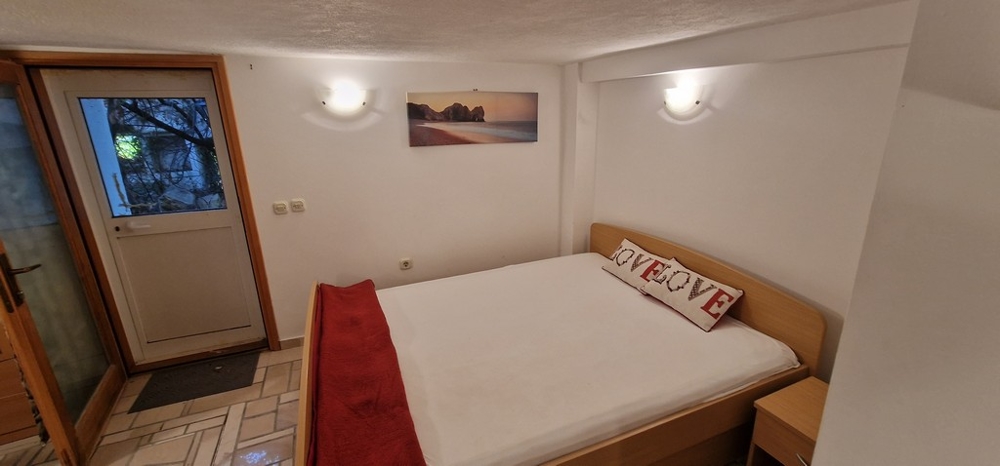 Una camera da letto con un letto matrimoniale decorato con accenti bianchi e rossi. Alla parete è appeso un quadro di una spiaggia e una porta conduce all'esterno.
