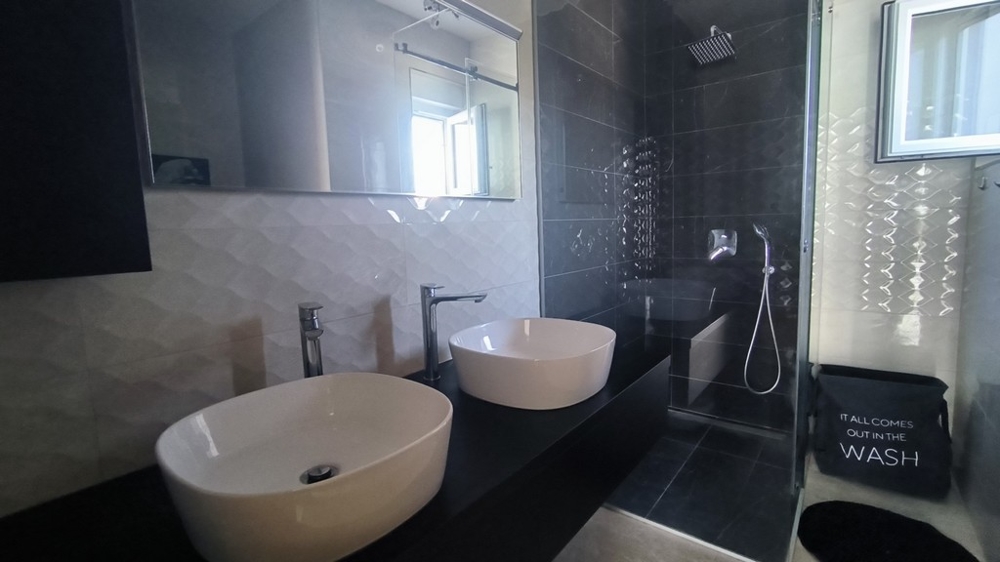 Bagno moderno con doppio lavabo e doccia a pioggia.