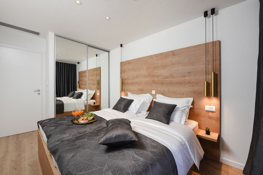 Camera da letto arredata in modo moderno con elementi in legno e armadio con ante scorrevoli a specchio.