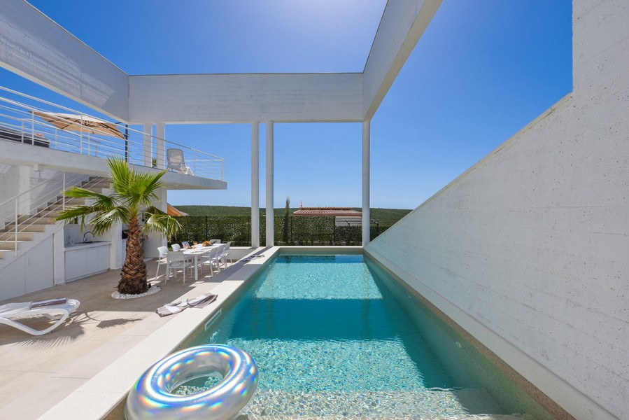 Piscina rettangolare con ampia terrazza e tavolo da pranzo all'aperto.