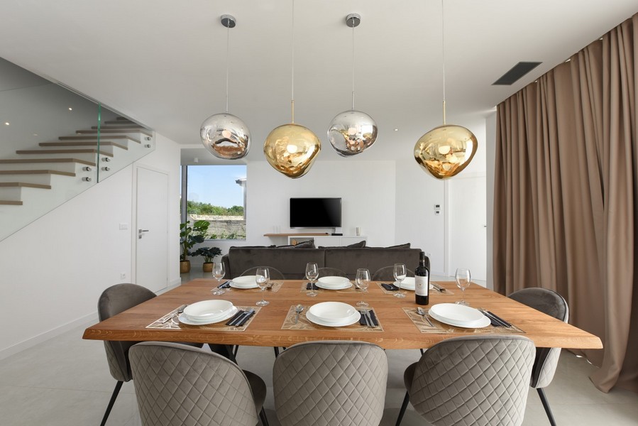 Zona pranzo moderna con tavolo in legno e lampade di design in un concetto abitativo aperto.