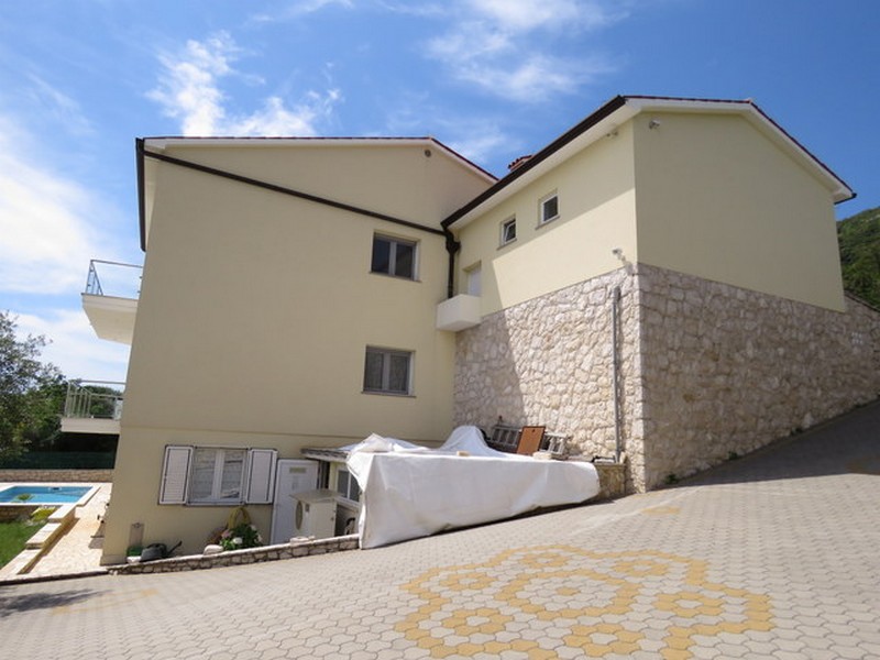 Vista esterna della casa con parcheggio pavimentato e piscina sullo sfondo.