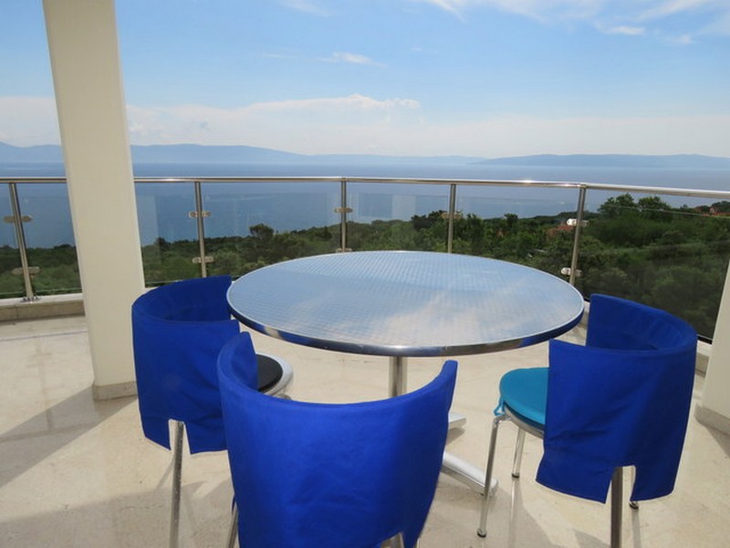 Balcone con bella vista mare e zona pranzo con sedie blu.