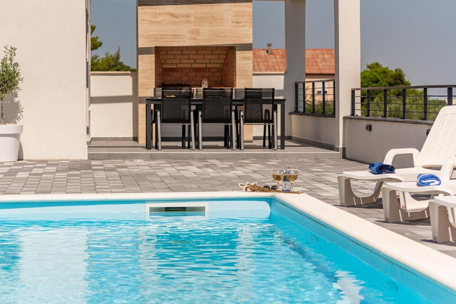 Area esterna con piscina, lettini prendisole e zona barbecue sullo sfondo.