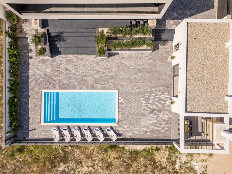 Veduta aerea della casa con ampia terrazza, piscina e moderne aree del giardino.