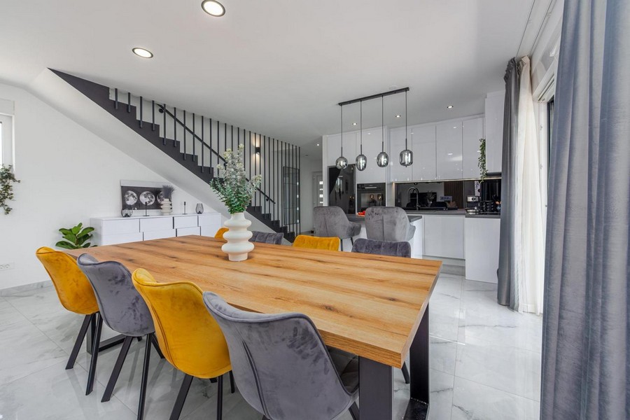 Zona pranzo con tavolo in legno, sedie colorate e cucina moderna sullo sfondo.