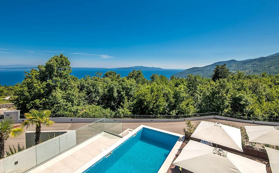 Piscina con ombrelloni e vista sul bosco fino al mare