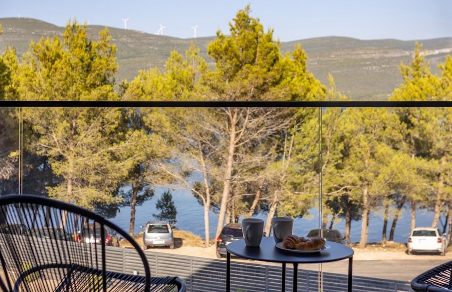 Tavolo sul balcone con cornetti e vista attraverso i pini sulla baia