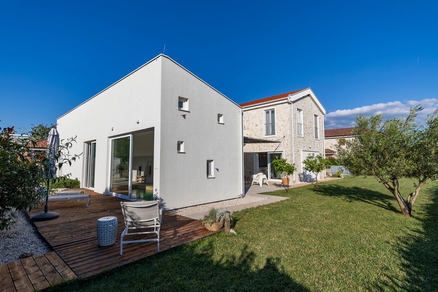 Deck in legno con lettini accanto all'annesso bianco in giardino