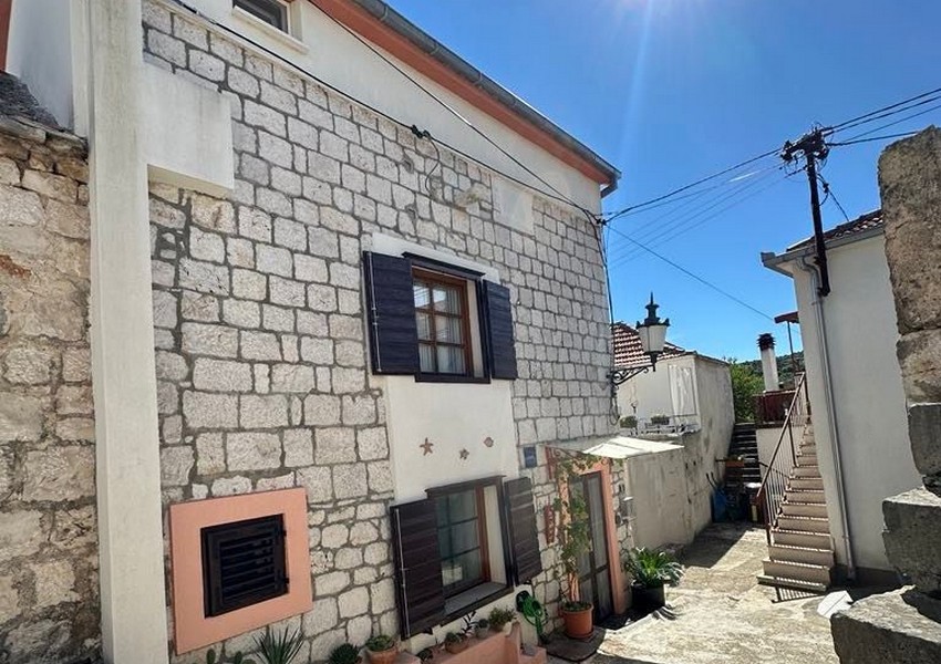 Casa in pietra con persiane scure e vasi di fiori nel vicolo