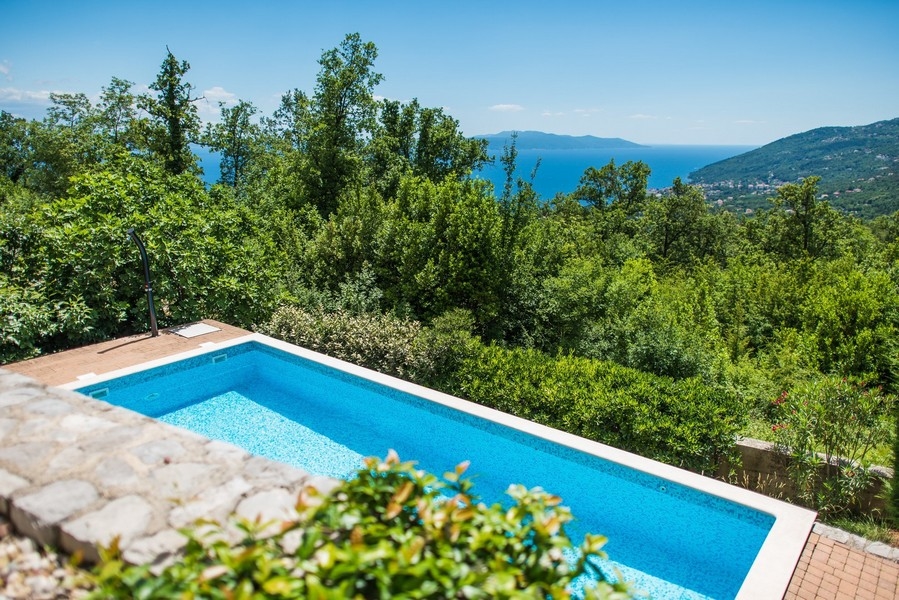 Piscina sopra il muro a secco con vista attraverso gli alberi sul mare