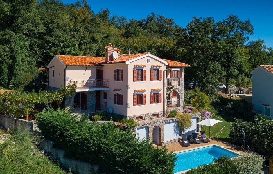 Villa rosa con tetto di tegole e piscina al margine del bosco