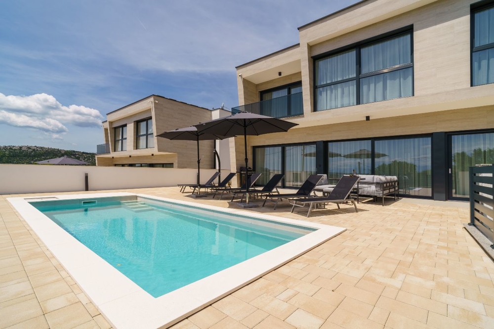Piscina con lettini e ombrelloni davanti alla villa chiara