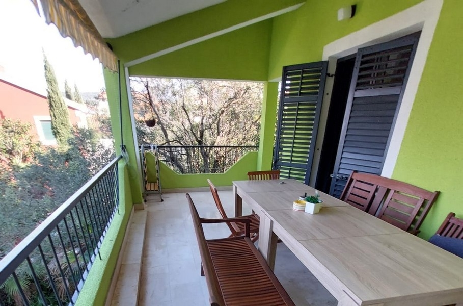 Loggia con lungo tavolo in legno davanti alla parete verde della casa