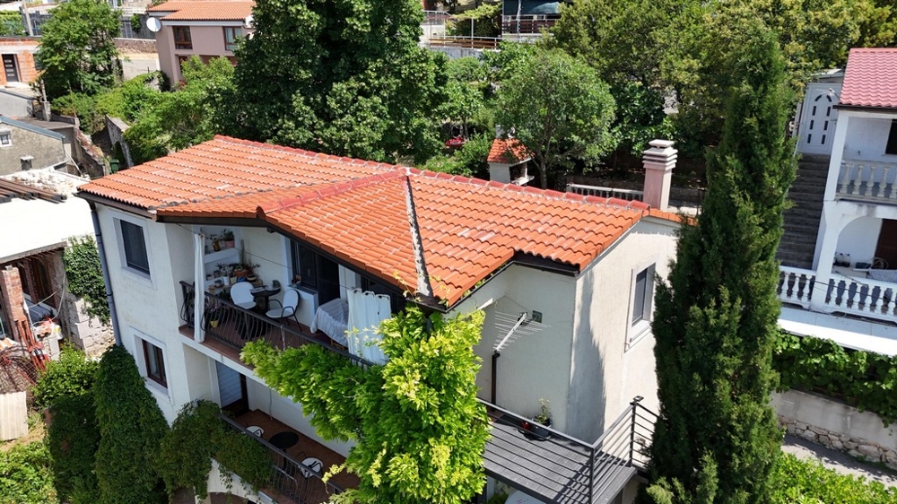 Casa con tetto in tegole e balcone tra il verde fitto