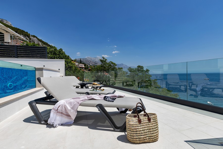 Lettini prendisole sulla terrazza con parapetto in vetro verso il mare