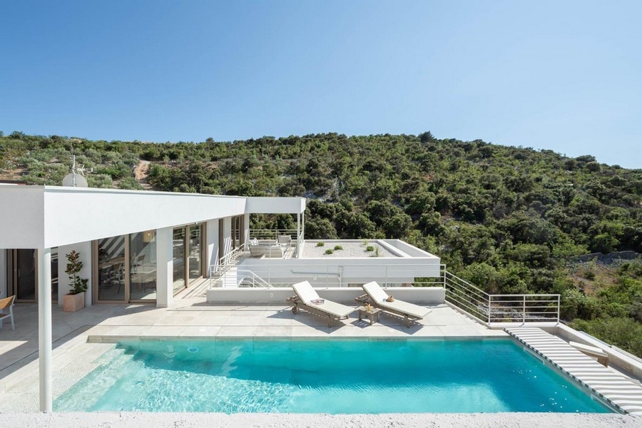 Casa bianca con piscina e lettini davanti al pendio ricoperto di vegetazione