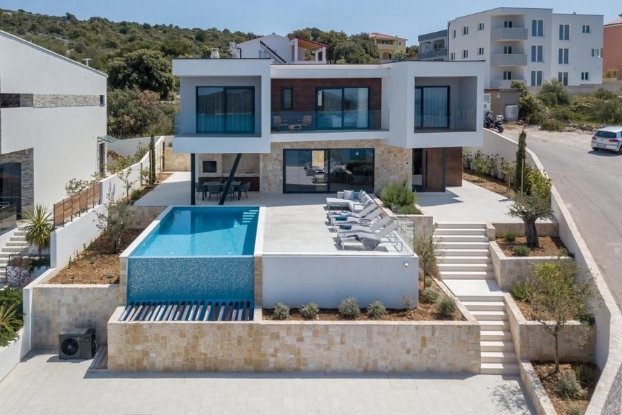 Villa con piscina a sfioro e fila di lettini sopra il muro a secco
