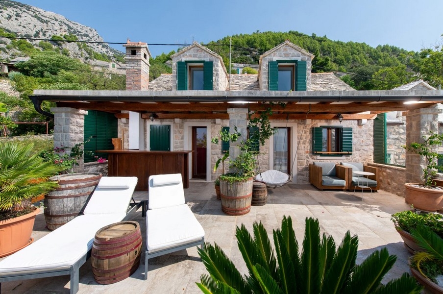 Casa in pietra con persiane verdi e lettini sotto la pergola
