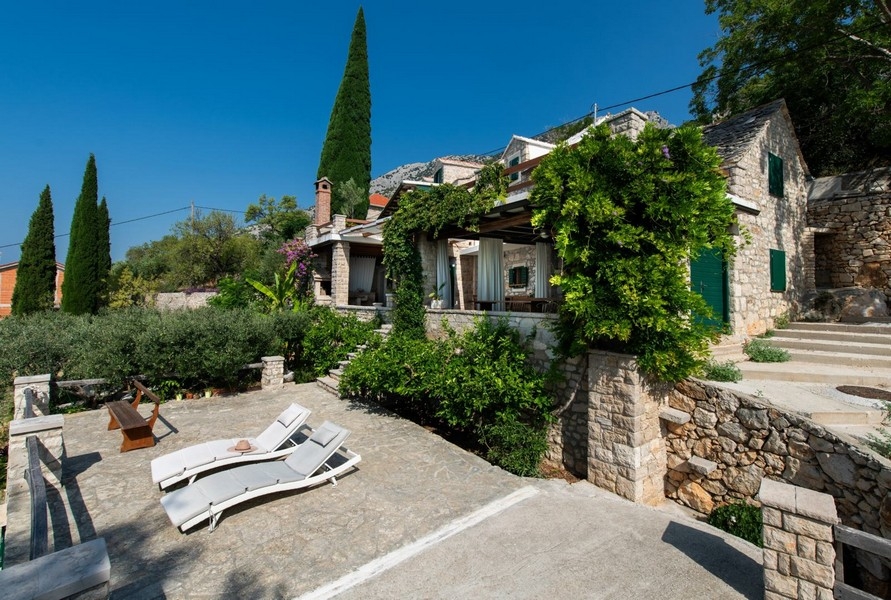 Casa in pietra con piante rampicanti e lettini sulla terrazza