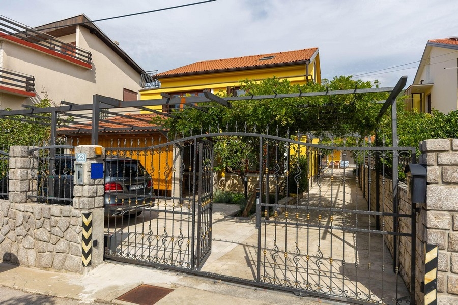 Ingresso carrabile del terreno con cancello e casa gialla