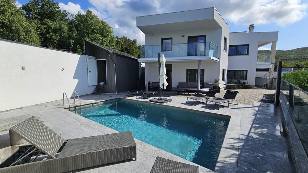 Piscina con lettini davanti alla villa bianca con balcone in vetro