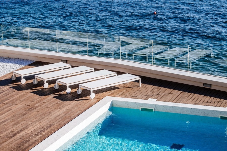 Lettini sulla piattaforma in legno tra piscina e mare
