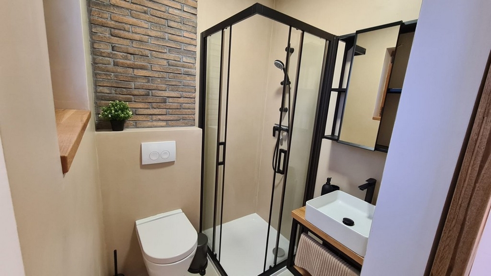 Bagno con doccia angolare e parete in mattoni sopra il lavabo
