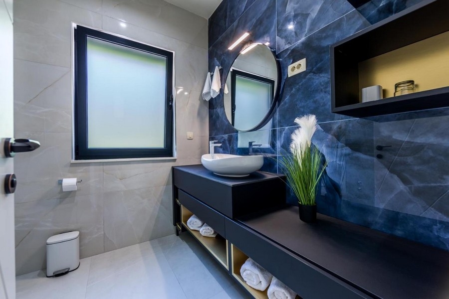 Bagno con parete in marmo blu e specchio rotondo