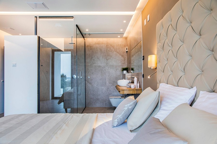 Camera da letto con bagno in vetro e testiera beige.
