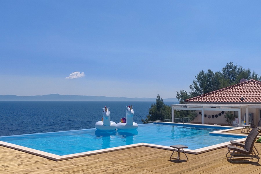 Piscina a sfioro con vista mare e ampia terrazza in legno