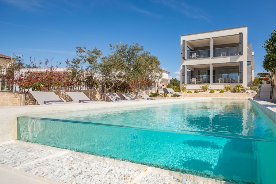 Piscina con parete in vetro e lettini davanti al moderno edificio nuovo