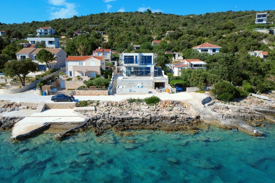 Veduta aerea della casa in vetro sulla riva rocciosa con acqua turchese