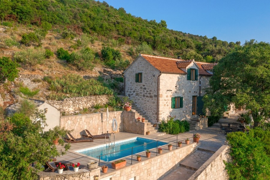 Casa in pietra con persiane verdi e piscina davanti al muretto a secco