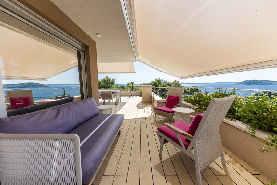 Terrazza con tenda da sole e poltrone rosa sopra la baia