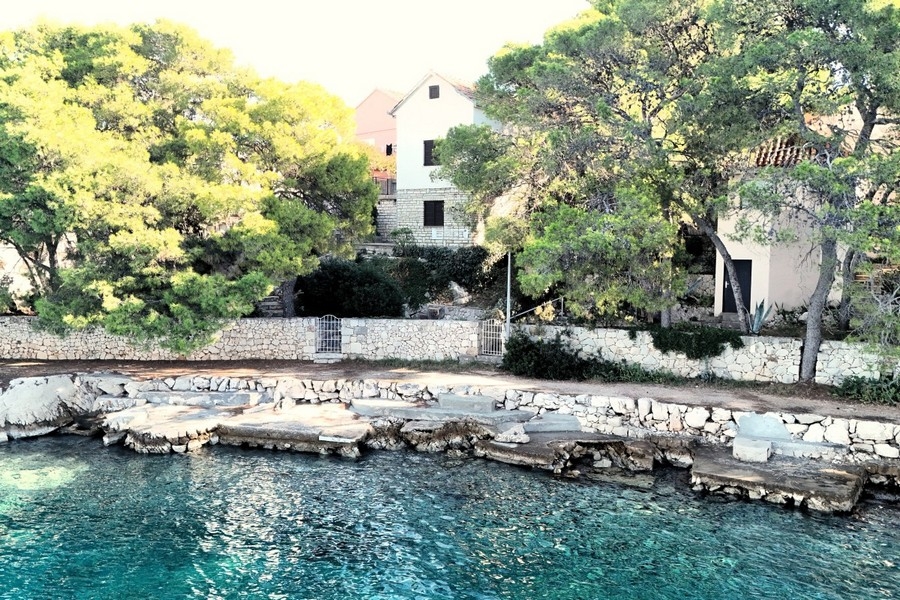 Casa dietro i pini sopra la costa rocciosa con acqua turchese