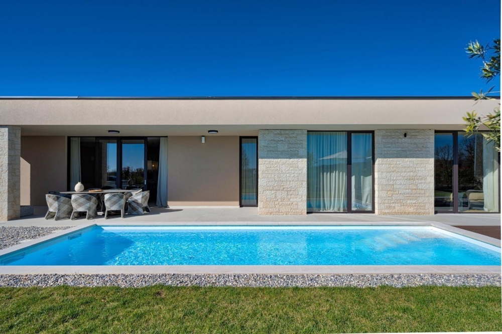 Casa con tetto piano e facciata in pietra naturale e piscina nel prato