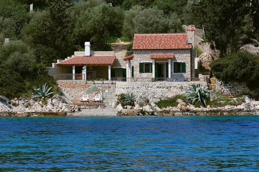 Casa in pietra con persiane verdi e agavi sulla riva rocciosa