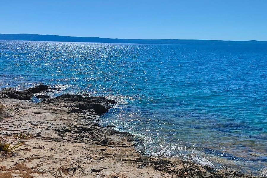 Costa rocciosa con acqua scintillante e isola all'orizzonte