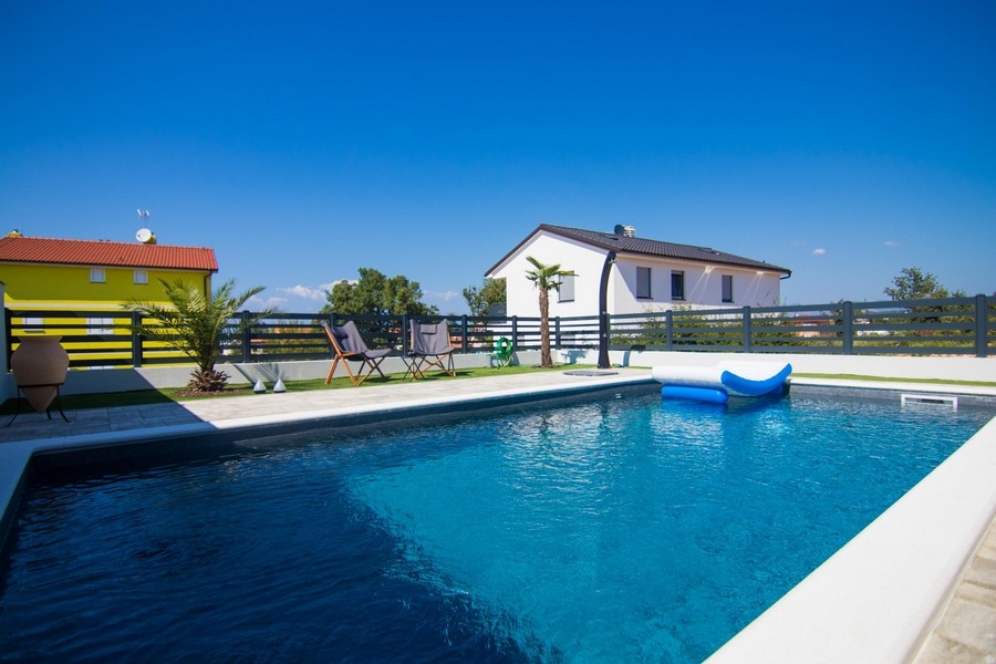 Piscina con materassino e palme davanti alla casa bianca