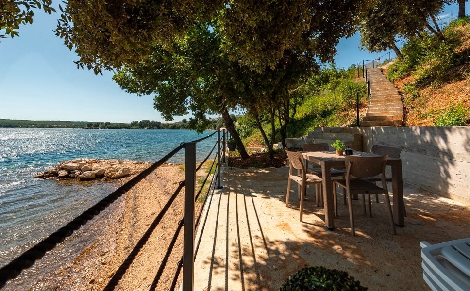 Tavolo da pranzo sulla riva sotto gli alberi con scala verso la casa