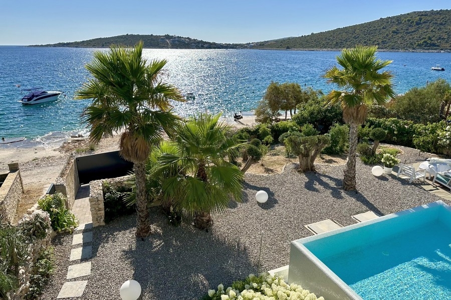 Spiaggia e mare direttamente davanti alla villa con piscina e giardino di palme