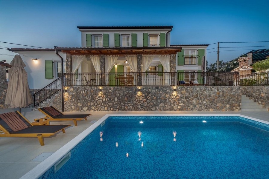 Villa illuminata con persiane verdi e piscina la sera