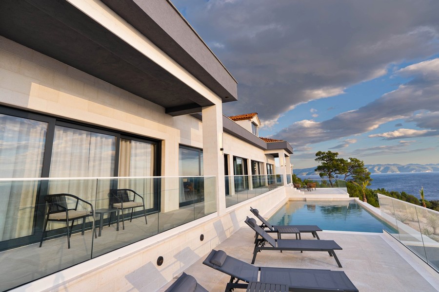 Terrazza con parapetto in vetro e lettini accanto alla piscina