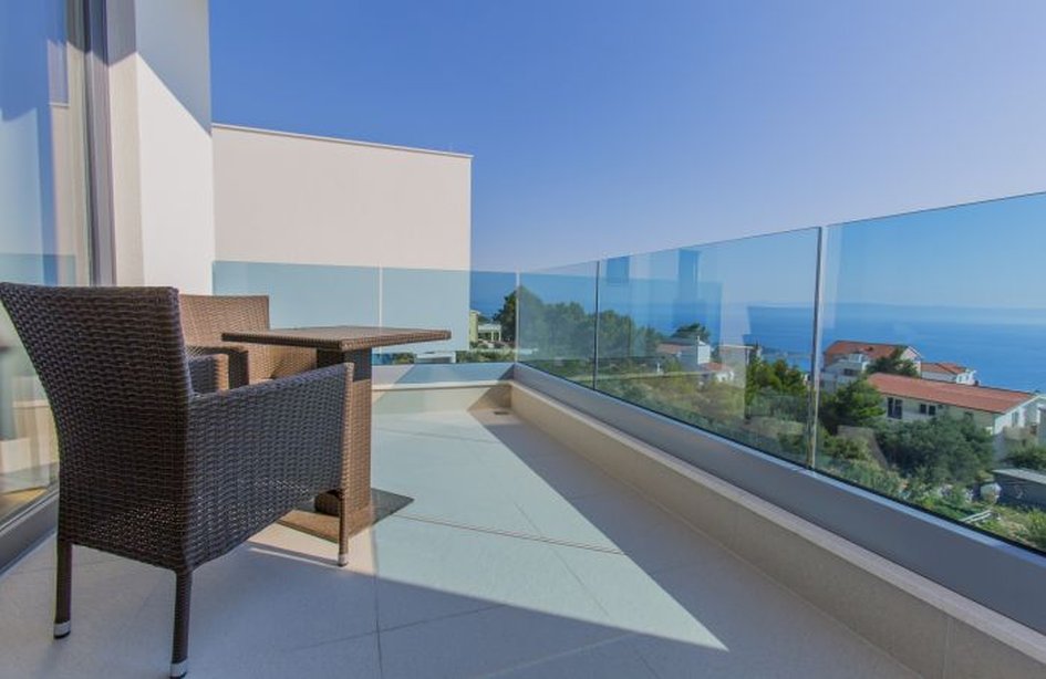 Balcone con parapetto in vetro e poltrona in vimini sopra la costa