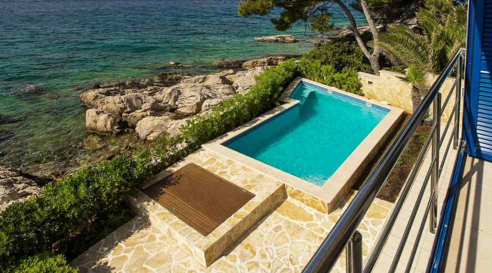 Piscina sopra la costa rocciosa con deck in legno e lastre di pietra naturale