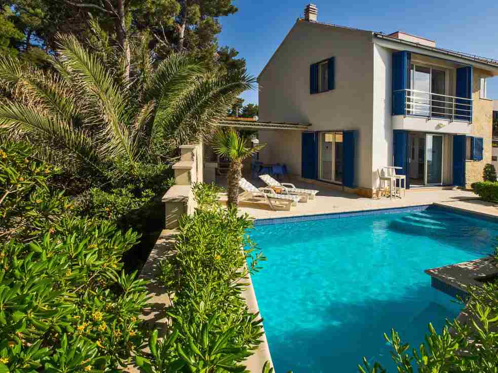 Casa con persiane blu e piscina dietro cespugli di oleandro