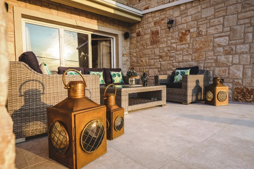 Terrazza con mobili in rattan e lanterne davanti alla parete in pietra naturale